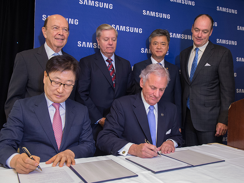 U.S. Secretary of Commerce Wilbur Ross (standing left), Senator Lindsey Graham (standing left center), Korean Vice Minister of Trade, Industry & Energy Inho Lee (standing right center), Samsung Electronics America President & CEO Tim Baxter (standing right), Samsung Electronics President & CEO of Consumer Electronics Boo-Keun Yoon (seated left) and South Carolina Governor Henry McMaster (seated right)