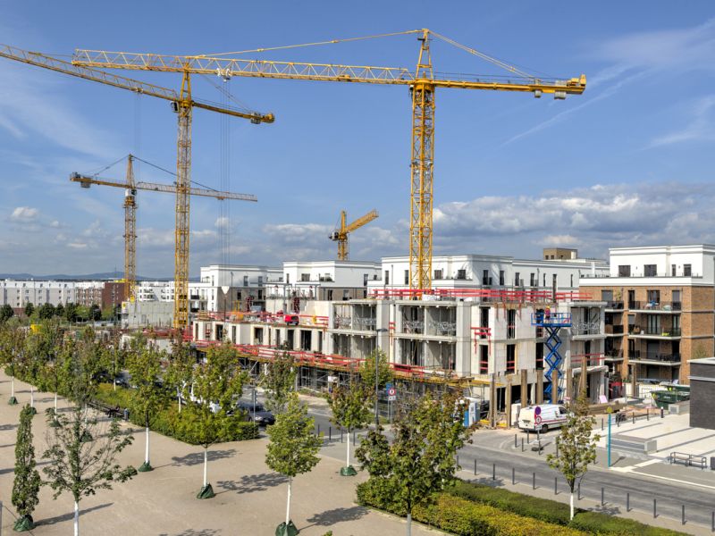 A new development area of residential buildings with construction cranes and construction site in the background