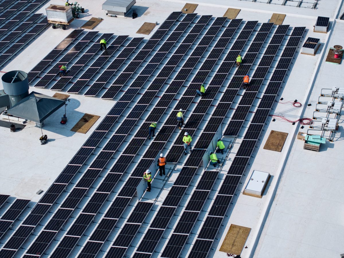 Photo of rooftop installation of solar panels on warehouse.