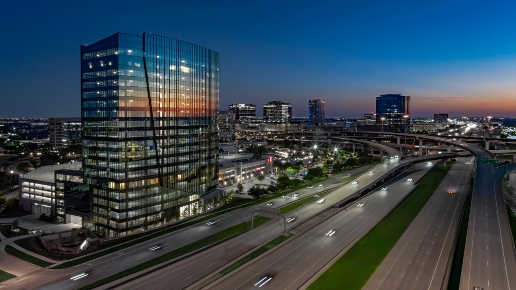 Aerial shot of Granite Park Six, a 19-story 422,109-square-foot office building in Plano, Texas. The image features the building overlooking Texas State Highway 121, at night.
