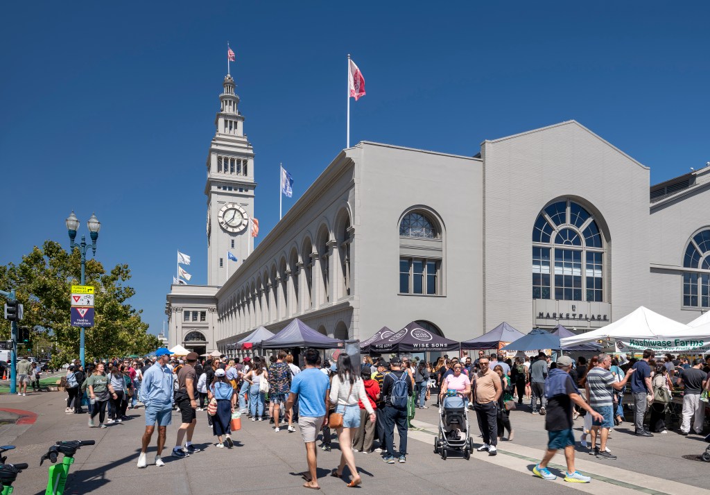 People walking around the farmers market, with part of the Ferry Building in the background