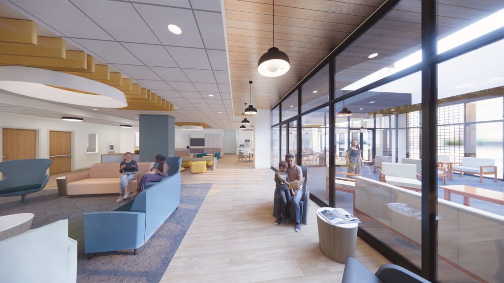 Second-floor lounge at The Wellness Village. Image features an large interior hallway with furniture pieces and people sitting around, as well as a large glass door that provides access to an adjacent area on the right.