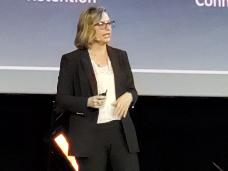 Woman wearing glasses and a blazer delivering a speech in front of a large screen