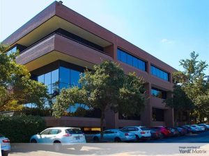 Exterior shot of Escalade Office Park, a two-building campus in Austin, Texas. Several cars and trees surrounding the building are visible in the frame