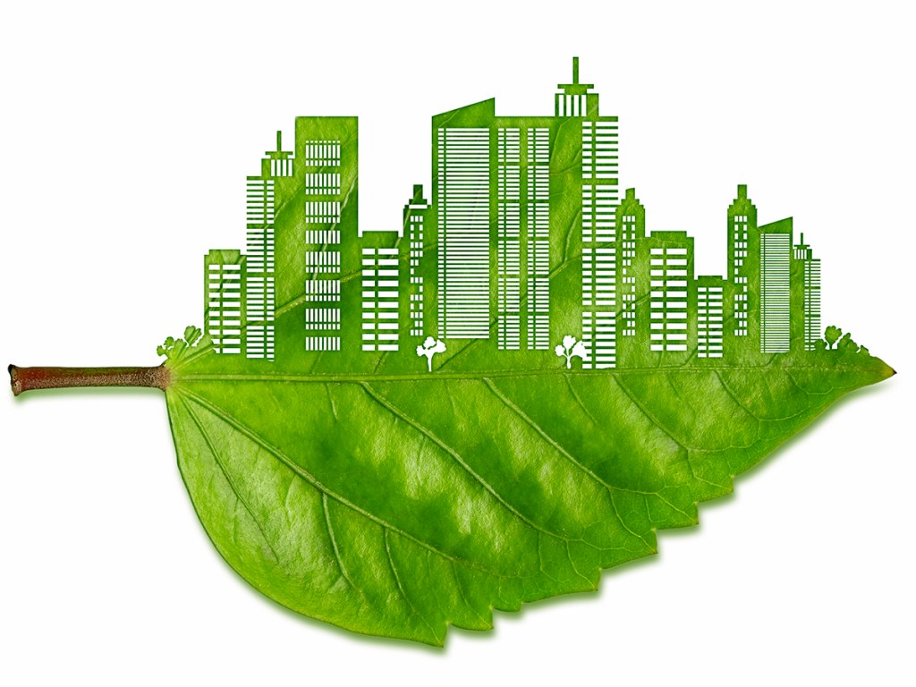 Top half of a green and fresh leaf is carved as the silhouette of a big city which is isolated on a white background. Carved part is showing a metropolis view with lots of high buildings and plazas.