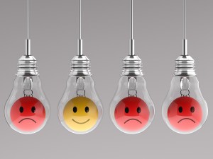 Four light bulbs with emoticons inside, three red and sad and one yellow and happy, hanging from the ceiling