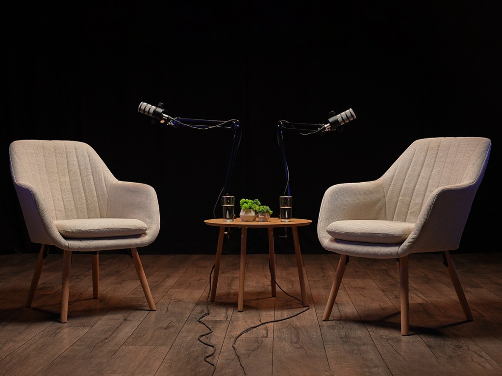 Cozy podcast setting with chairs and microphones, black background