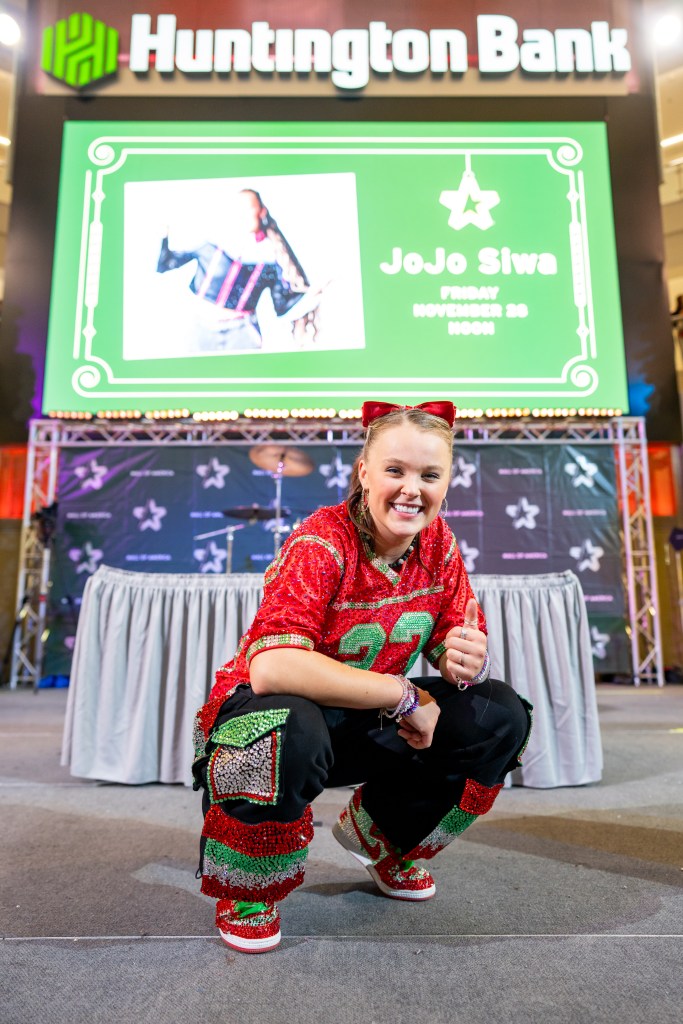 Full shot of Jojo Siwa in front of a panel and table