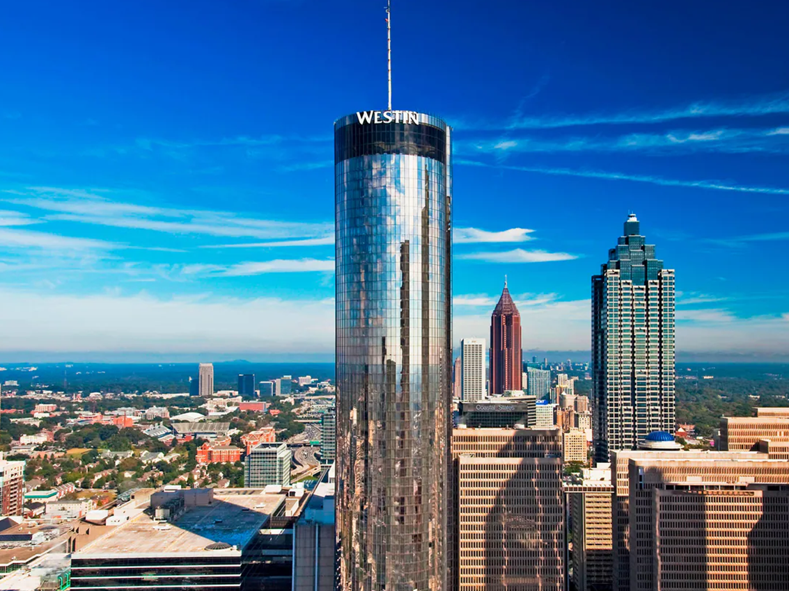 Exterior, aerial shot of the Westin Peachtree Plaza hotel in downtown Atlanta. The building has a cylindrical shape and reflective glass facade