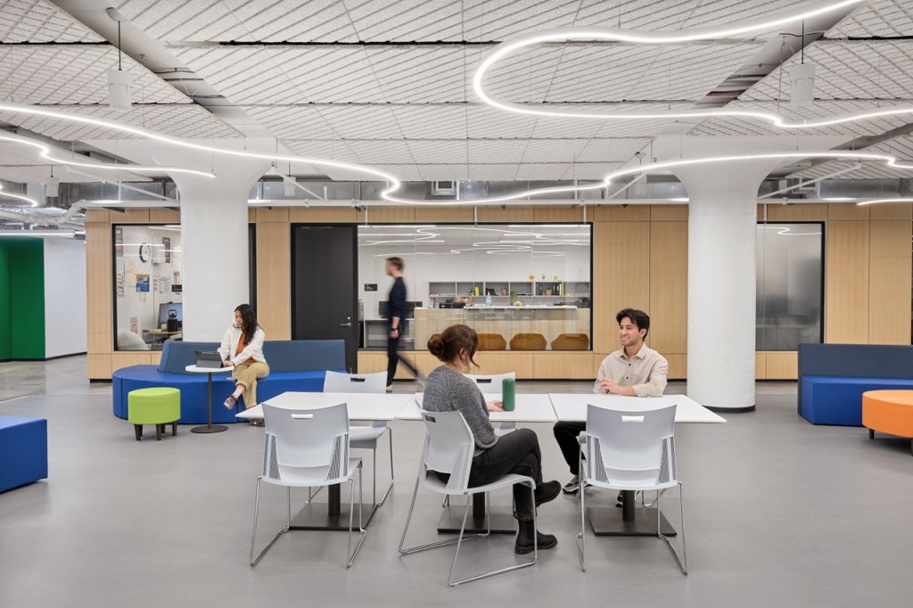 A group of people collaborating at tables in a modern open office space, engaged in discussion and teamwork.