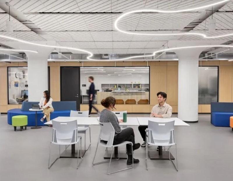 A group of people collaborating at tables in a modern open office space, engaged in discussion and teamwork.