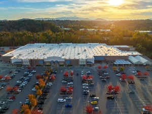 Aerial view of large parking lot in front of rgocery store with many parked colorful cars. Carpark at supercenter shopping mall with lines and markings for vehicle places and directions.